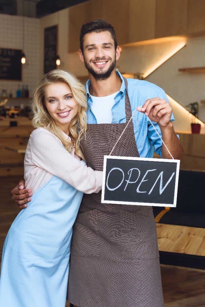 cheerful-young-cafe-owners-holding-sign-open-and-s-2021-09-03-11-15-01-utc-1