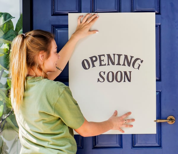 woman-putting-on-store-opening-soon-sign-2023-11-27-05-27-56-utc-1
